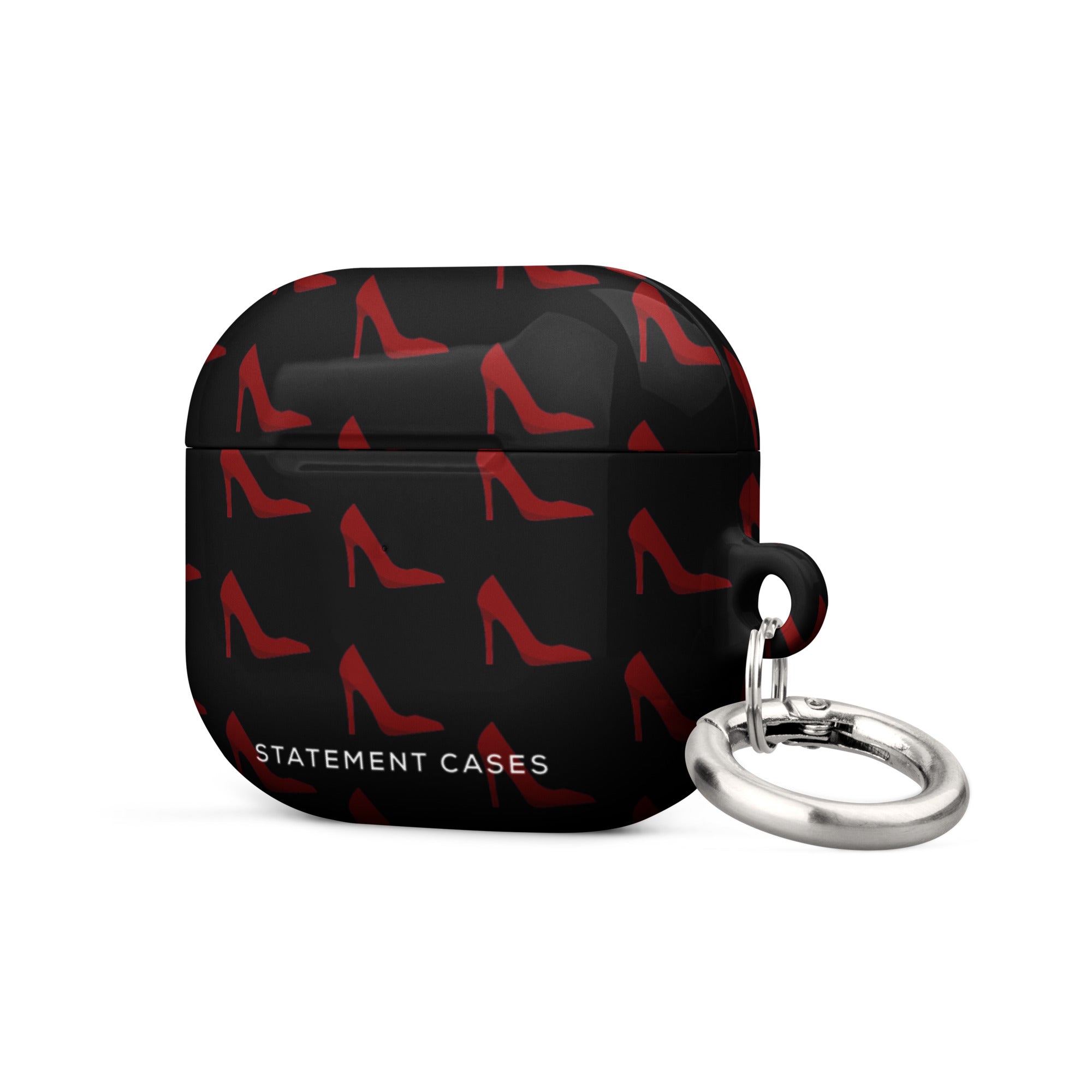 A black Saucy Stillettos for AirPods Gen 3 adorned with a pattern of red high-heeled shoes. It is branded with "Statement Cases" in white text on the front. The impact-absorbing case has a metal carabiner attached to the side for convenience.
