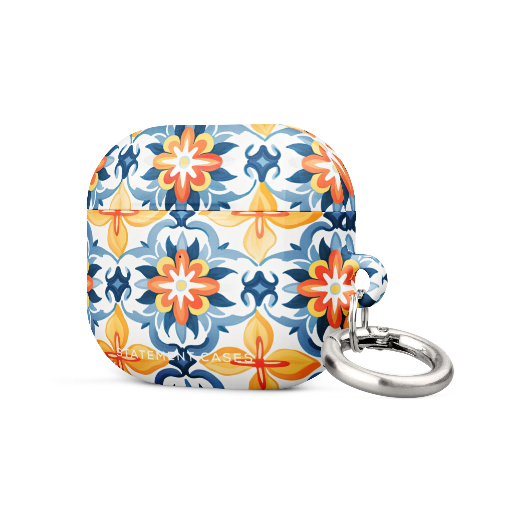 A rectangular AirPods case with a metal carabiner attachment, featuring an impact-absorbing design and a vibrant floral and geometric pattern in blue, orange, yellow, and white colors reminiscent of traditional tile designs. The brand name "Statement Cases" is printed on the bottom. This is the Mediterranean Bloom for AirPods Gen 3.