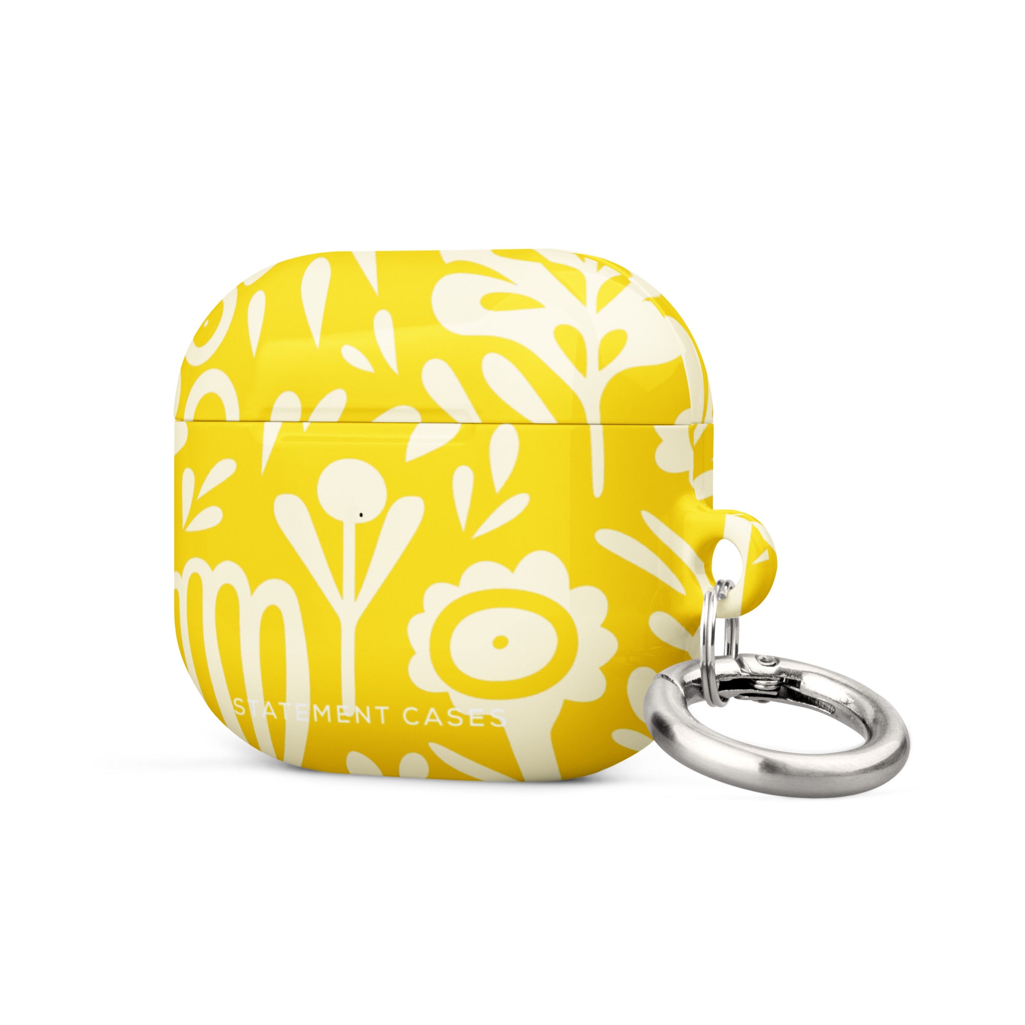 The Sol Dorado for AirPods Gen 3 by Statement Cases features a bright yellow design with white floral and abstract patterns. It offers a sturdy, impact-absorbing construction and comes with a metallic keyring on the right side for easy attachment to bags or keychains. The brand name "Statement Cases" is subtly printed on the front.