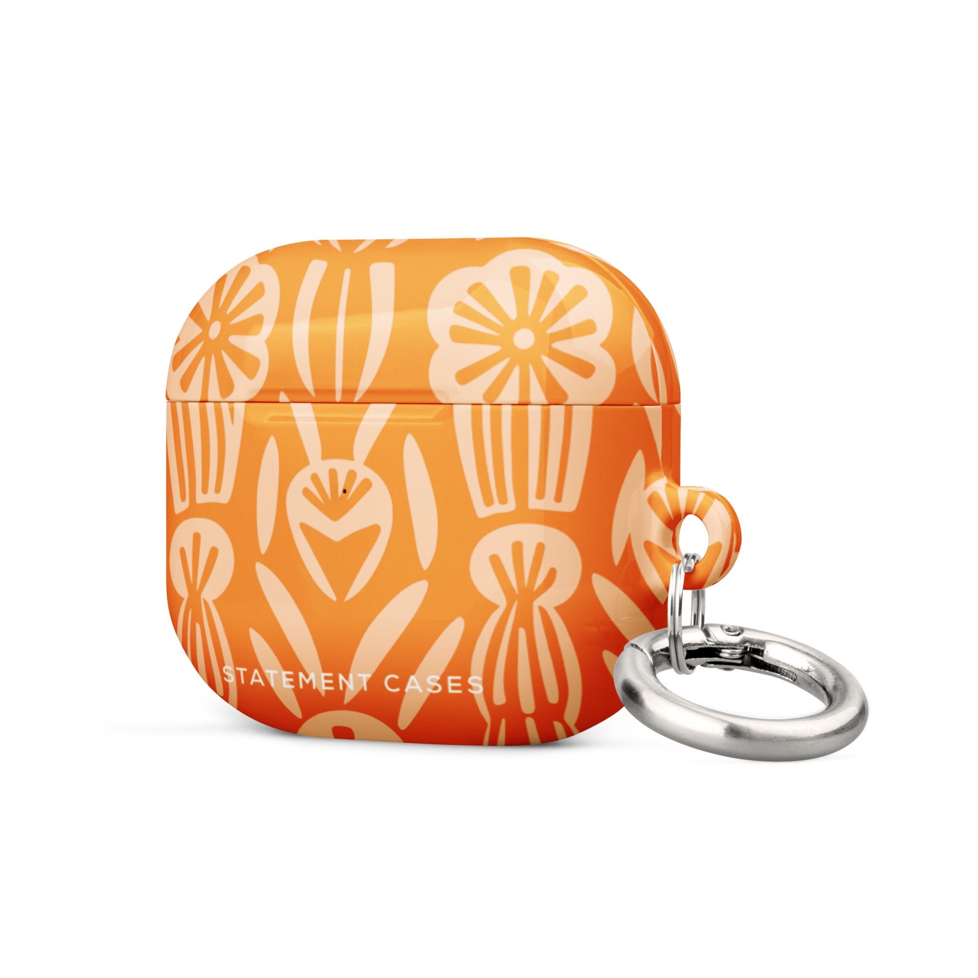 The Savannah Ardiente for AirPods Gen 3 by Statement Cases showcases a vibrant cream floral pattern set against an orange background. Crafted from premium impact-absorbing material, the design highlights abstract flowers and foliage. A small metal carabiner with a detachable keyring is affixed to the right side, and "STATEMENT CASES" is printed in white at the bottom.