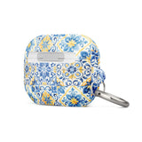 The Blue Mirage for AirPods Pro Gen 2 by Statement Cases is a decorative case for wireless earbuds, featuring an intricate blue and yellow tile pattern inspired by traditional Portuguese azulejos. This impact-absorbing case includes a small metal carabiner for easy attachment.