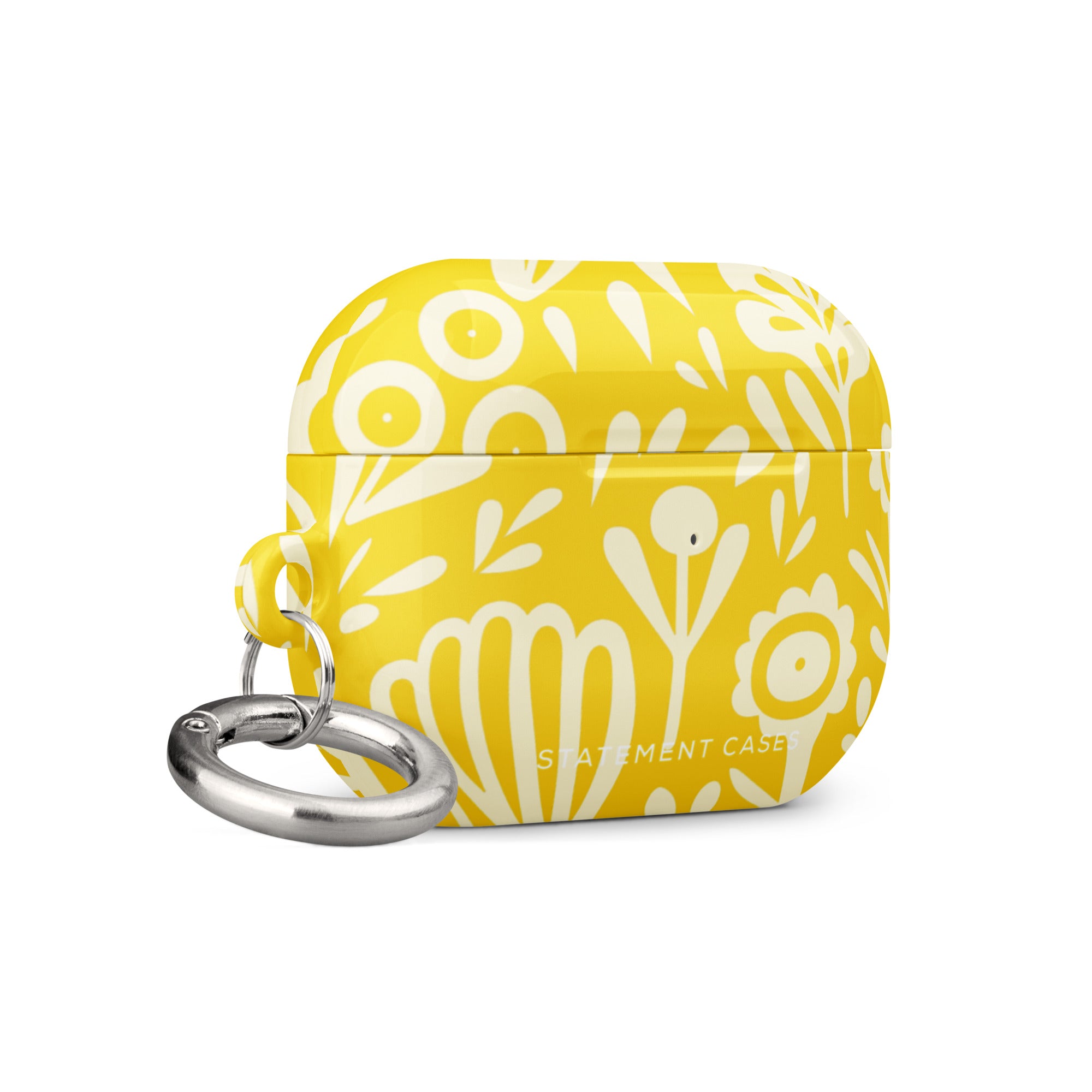 Introducing the Sol Dorado for AirPods Pro Gen 2 from Statement Cases: a yellow AirPods case adorned with a white floral and leaf pattern. This case includes a metal carabiner for easy attachment and is engineered to be impact-absorbing. The brand name "Statement Cases" is printed in small white letters at the bottom center.