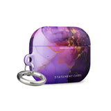 The Golden Orchid Marble for AirPods Pro Gen 2 by Statement Cases features an abstract, swirling pattern in shades of purple and gold, with "STATEMENT CASES" emblazoned on the front. It comes with a metal carabiner for easy carrying and has a premium impact-absorbing design to protect your AirPods.