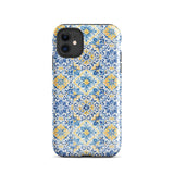 The Blue Mirage for iPhone by Statement Cases features a dual-layered, impact-resistant polycarbonate exterior with a TPU inner liner. Inspired by traditional Portuguese tiles, the blue and yellow patterned case boasts an intricate design of floral and geometric motifs. With its elegant and colorful appearance, the phone's camera is visible at the top left of the case.