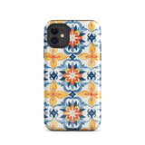 Statement Cases' Mediterranean Bloom for iPhone is showcased, featuring an intricate, colorful pattern. The design includes blue, yellow, and orange floral shapes in a symmetrical arrangement on a light blue background. This durable phone case provides dual-layer protection and is constructed from impact-resistant polycarbonate to safeguard your device.