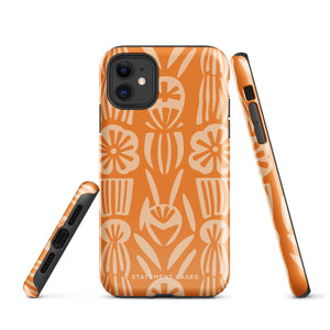 A Savannah Ardiente for iPhone from Statement Cases, featuring a dual-layered phone case in orange with a floral pattern showcasing cream-colored flowers, leaves, and geometric shapes. This impact-resistant polycarbonate case displays "STATEMENT CASES" at the bottom and reveals the camera lenses at the top left corner.