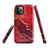 A smartphone in a protective Scarlet Marble for iPhone case by Statement Cases with a red and gold marbled abstract design. The case has "Statement Cases" written at the bottom. The iPhone 15 Pro Max features three camera lenses and a flash on the top left corner.