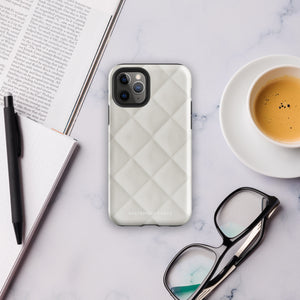 A smartphone with a textured, light gray Quilted Delight for iPhone protective case is shown. The case has a camera cutout that fits three lenses and a flash, with "Statement Cases" written at the bottom, perfectly tailored for the iPhone 15 Pro Max.