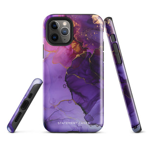 A Statement Cases Golden Orchid Marble for iPhone with a case featuring an abstract design of swirling purple, pink, and gold hues over a white background. The marbled patterns with metallic accents provide dual-layer protection and are impact-resistant. The top of the case has cutouts for the phone's camera lenses and is induction charging compatible.