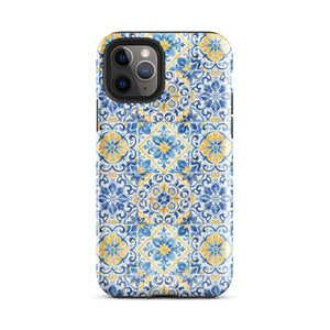 The Blue Mirage for iPhone by Statement Cases features a dual-layered, impact-resistant polycarbonate exterior with a TPU inner liner. Inspired by traditional Portuguese tiles, the blue and yellow patterned case boasts an intricate design of floral and geometric motifs. With its elegant and colorful appearance, the phone's camera is visible at the top left of the case.