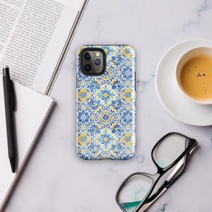 The Blue Mirage for iPhone by Statement Cases features a dual-layered, impact-resistant polycarbonate exterior with a TPU inner liner. Inspired by traditional Portuguese tiles, the blue and yellow patterned case boasts an intricate design of floral and geometric motifs. With its elegant and colorful appearance, the phone's camera is visible at the top left of the case.