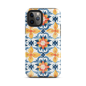 Statement Cases' Mediterranean Bloom for iPhone is showcased, featuring an intricate, colorful pattern. The design includes blue, yellow, and orange floral shapes in a symmetrical arrangement on a light blue background. This durable phone case provides dual-layer protection and is constructed from impact-resistant polycarbonate to safeguard your device.