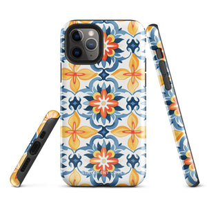 Statement Cases' Mediterranean Bloom for iPhone is showcased, featuring an intricate, colorful pattern. The design includes blue, yellow, and orange floral shapes in a symmetrical arrangement on a light blue background. This durable phone case provides dual-layer protection and is constructed from impact-resistant polycarbonate to safeguard your device.