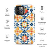 Statement Cases' Mediterranean Bloom for iPhone is showcased, featuring an intricate, colorful pattern. The design includes blue, yellow, and orange floral shapes in a symmetrical arrangement on a light blue background. This durable phone case provides dual-layer protection and is constructed from impact-resistant polycarbonate to safeguard your device.