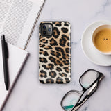 A smartphone with a Mighty Jaguar Fur for iPhone protective case by Statement Cases. The design features a classic leopard fur pattern with black spots on a tan and brown background. The camera lenses of the iPhone 15 Pro Max are clearly visible at the top left corner of the phone. The word "Statement." is partially visible at the bottom.
