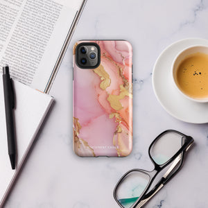 The Gold Blush Marble for iPhone showcases a glossy, marble-patterned case in shades of pink and gold. The decorative design features swirling patterns, seamlessly blending the colors. Crafted with impact-resistant polycarbonate for superior phone protection, "Statement Cases" is written in white at the bottom.