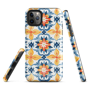 Statement Cases' Mediterranean Bloom for iPhone is showcased, featuring an intricate, colorful pattern. The design includes blue, yellow, and orange floral shapes in a symmetrical arrangement on a light blue background. This durable phone case provides dual-layer protection and is constructed from impact-resistant polycarbonate to safeguard your device.