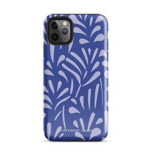 An iPhone encased in the "Mariposa Azul" by Statement Cases, featuring a blue design with an abstract white leaf pattern. The case combines curved and pointed shapes and provides dual-layer protection with TPU lining and impact-resistant polycarbonate. Camera lenses and other top elements remain unobstructed, and "Statement Cases" is inscribed at the bottom.