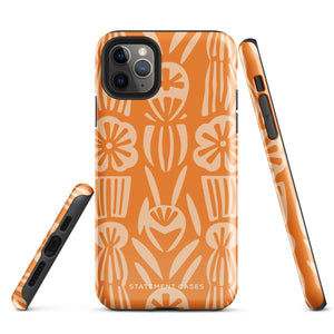 A Savannah Ardiente for iPhone from Statement Cases, featuring a dual-layered phone case in orange with a floral pattern showcasing cream-colored flowers, leaves, and geometric shapes. This impact-resistant polycarbonate case displays "STATEMENT CASES" at the bottom and reveals the camera lenses at the top left corner.