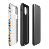 Statement Cases' Mediterranean Bloom for iPhone is showcased, featuring an intricate, colorful pattern. The design includes blue, yellow, and orange floral shapes in a symmetrical arrangement on a light blue background. This durable phone case provides dual-layer protection and is constructed from impact-resistant polycarbonate to safeguard your device.