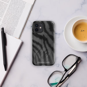 A Charisma Tiger Fur for iPhone with a black and gray striped case featuring a glossy, brushed metal texture. This protective iPhone case, compatible with the iPhone 15 Pro Max, is branded "Statement Cases" at the bottom. The phone's camera lenses are visible in the top left corner.
