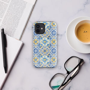 The Blue Mirage for iPhone by Statement Cases features a dual-layered, impact-resistant polycarbonate exterior with a TPU inner liner. Inspired by traditional Portuguese tiles, the blue and yellow patterned case boasts an intricate design of floral and geometric motifs. With its elegant and colorful appearance, the phone's camera is visible at the top left of the case.