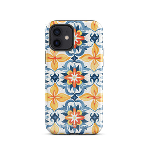 Statement Cases' Mediterranean Bloom for iPhone is showcased, featuring an intricate, colorful pattern. The design includes blue, yellow, and orange floral shapes in a symmetrical arrangement on a light blue background. This durable phone case provides dual-layer protection and is constructed from impact-resistant polycarbonate to safeguard your device.