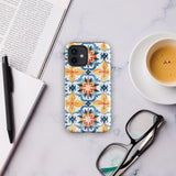 Statement Cases' Mediterranean Bloom for iPhone is showcased, featuring an intricate, colorful pattern. The design includes blue, yellow, and orange floral shapes in a symmetrical arrangement on a light blue background. This durable phone case provides dual-layer protection and is constructed from impact-resistant polycarbonate to safeguard your device.