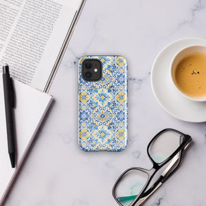 The Blue Mirage for iPhone by Statement Cases features a dual-layered, impact-resistant polycarbonate exterior with a TPU inner liner. Inspired by traditional Portuguese tiles, the blue and yellow patterned case boasts an intricate design of floral and geometric motifs. With its elegant and colorful appearance, the phone's camera is visible at the top left of the case.