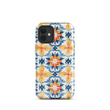 Statement Cases' Mediterranean Bloom for iPhone is showcased, featuring an intricate, colorful pattern. The design includes blue, yellow, and orange floral shapes in a symmetrical arrangement on a light blue background. This durable phone case provides dual-layer protection and is constructed from impact-resistant polycarbonate to safeguard your device.