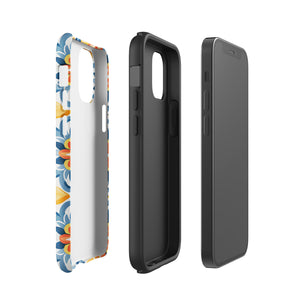 Statement Cases' Mediterranean Bloom for iPhone is showcased, featuring an intricate, colorful pattern. The design includes blue, yellow, and orange floral shapes in a symmetrical arrangement on a light blue background. This durable phone case provides dual-layer protection and is constructed from impact-resistant polycarbonate to safeguard your device.