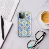 The Blue Mirage for iPhone by Statement Cases features a dual-layered, impact-resistant polycarbonate exterior with a TPU inner liner. Inspired by traditional Portuguese tiles, the blue and yellow patterned case boasts an intricate design of floral and geometric motifs. With its elegant and colorful appearance, the phone's camera is visible at the top left of the case.