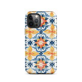 Statement Cases' Mediterranean Bloom for iPhone is showcased, featuring an intricate, colorful pattern. The design includes blue, yellow, and orange floral shapes in a symmetrical arrangement on a light blue background. This durable phone case provides dual-layer protection and is constructed from impact-resistant polycarbonate to safeguard your device.