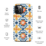 Statement Cases' Mediterranean Bloom for iPhone is showcased, featuring an intricate, colorful pattern. The design includes blue, yellow, and orange floral shapes in a symmetrical arrangement on a light blue background. This durable phone case provides dual-layer protection and is constructed from impact-resistant polycarbonate to safeguard your device.