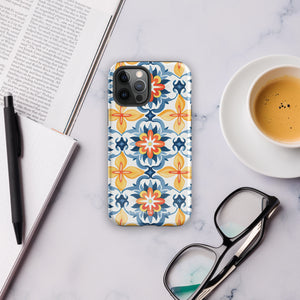 Statement Cases' Mediterranean Bloom for iPhone is showcased, featuring an intricate, colorful pattern. The design includes blue, yellow, and orange floral shapes in a symmetrical arrangement on a light blue background. This durable phone case provides dual-layer protection and is constructed from impact-resistant polycarbonate to safeguard your device.