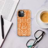 A Savannah Ardiente for iPhone from Statement Cases, featuring a dual-layered phone case in orange with a floral pattern showcasing cream-colored flowers, leaves, and geometric shapes. This impact-resistant polycarbonate case displays "STATEMENT CASES" at the bottom and reveals the camera lenses at the top left corner.