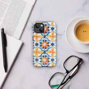 Statement Cases' Mediterranean Bloom for iPhone is showcased, featuring an intricate, colorful pattern. The design includes blue, yellow, and orange floral shapes in a symmetrical arrangement on a light blue background. This durable phone case provides dual-layer protection and is constructed from impact-resistant polycarbonate to safeguard your device.