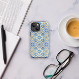 The Blue Mirage for iPhone by Statement Cases features a dual-layered, impact-resistant polycarbonate exterior with a TPU inner liner. Inspired by traditional Portuguese tiles, the blue and yellow patterned case boasts an intricate design of floral and geometric motifs. With its elegant and colorful appearance, the phone's camera is visible at the top left of the case.