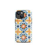 Statement Cases' Mediterranean Bloom for iPhone is showcased, featuring an intricate, colorful pattern. The design includes blue, yellow, and orange floral shapes in a symmetrical arrangement on a light blue background. This durable phone case provides dual-layer protection and is constructed from impact-resistant polycarbonate to safeguard your device.