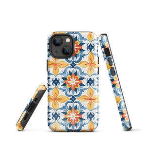 Statement Cases' Mediterranean Bloom for iPhone is showcased, featuring an intricate, colorful pattern. The design includes blue, yellow, and orange floral shapes in a symmetrical arrangement on a light blue background. This durable phone case provides dual-layer protection and is constructed from impact-resistant polycarbonate to safeguard your device.