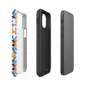 Statement Cases' Mediterranean Bloom for iPhone is showcased, featuring an intricate, colorful pattern. The design includes blue, yellow, and orange floral shapes in a symmetrical arrangement on a light blue background. This durable phone case provides dual-layer protection and is constructed from impact-resistant polycarbonate to safeguard your device.