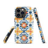 Statement Cases' Mediterranean Bloom for iPhone is showcased, featuring an intricate, colorful pattern. The design includes blue, yellow, and orange floral shapes in a symmetrical arrangement on a light blue background. This durable phone case provides dual-layer protection and is constructed from impact-resistant polycarbonate to safeguard your device.