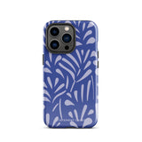 An iPhone encased in the "Mariposa Azul" by Statement Cases, featuring a blue design with an abstract white leaf pattern. The case combines curved and pointed shapes and provides dual-layer protection with TPU lining and impact-resistant polycarbonate. Camera lenses and other top elements remain unobstructed, and "Statement Cases" is inscribed at the bottom.