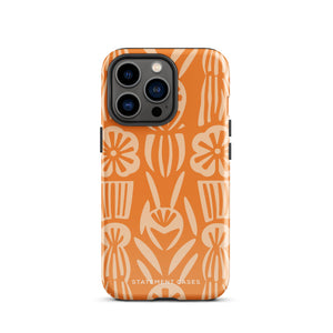 A Savannah Ardiente for iPhone from Statement Cases, featuring a dual-layered phone case in orange with a floral pattern showcasing cream-colored flowers, leaves, and geometric shapes. This impact-resistant polycarbonate case displays "STATEMENT CASES" at the bottom and reveals the camera lenses at the top left corner.