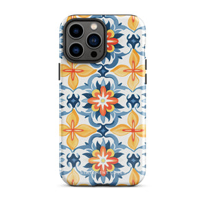 Statement Cases' Mediterranean Bloom for iPhone is showcased, featuring an intricate, colorful pattern. The design includes blue, yellow, and orange floral shapes in a symmetrical arrangement on a light blue background. This durable phone case provides dual-layer protection and is constructed from impact-resistant polycarbonate to safeguard your device.