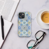 The Blue Mirage for iPhone by Statement Cases features a dual-layered, impact-resistant polycarbonate exterior with a TPU inner liner. Inspired by traditional Portuguese tiles, the blue and yellow patterned case boasts an intricate design of floral and geometric motifs. With its elegant and colorful appearance, the phone's camera is visible at the top left of the case.