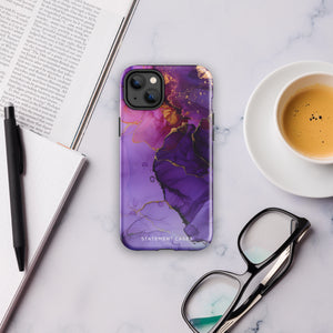 A Statement Cases Golden Orchid Marble for iPhone with a case featuring an abstract design of swirling purple, pink, and gold hues over a white background. The marbled patterns with metallic accents provide dual-layer protection and are impact-resistant. The top of the case has cutouts for the phone's camera lenses and is induction charging compatible.