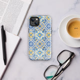 The Blue Mirage for iPhone by Statement Cases features a dual-layered, impact-resistant polycarbonate exterior with a TPU inner liner. Inspired by traditional Portuguese tiles, the blue and yellow patterned case boasts an intricate design of floral and geometric motifs. With its elegant and colorful appearance, the phone's camera is visible at the top left of the case.