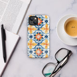 Statement Cases' Mediterranean Bloom for iPhone is showcased, featuring an intricate, colorful pattern. The design includes blue, yellow, and orange floral shapes in a symmetrical arrangement on a light blue background. This durable phone case provides dual-layer protection and is constructed from impact-resistant polycarbonate to safeguard your device.