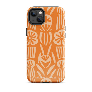 A Savannah Ardiente for iPhone from Statement Cases, featuring a dual-layered phone case in orange with a floral pattern showcasing cream-colored flowers, leaves, and geometric shapes. This impact-resistant polycarbonate case displays "STATEMENT CASES" at the bottom and reveals the camera lenses at the top left corner.